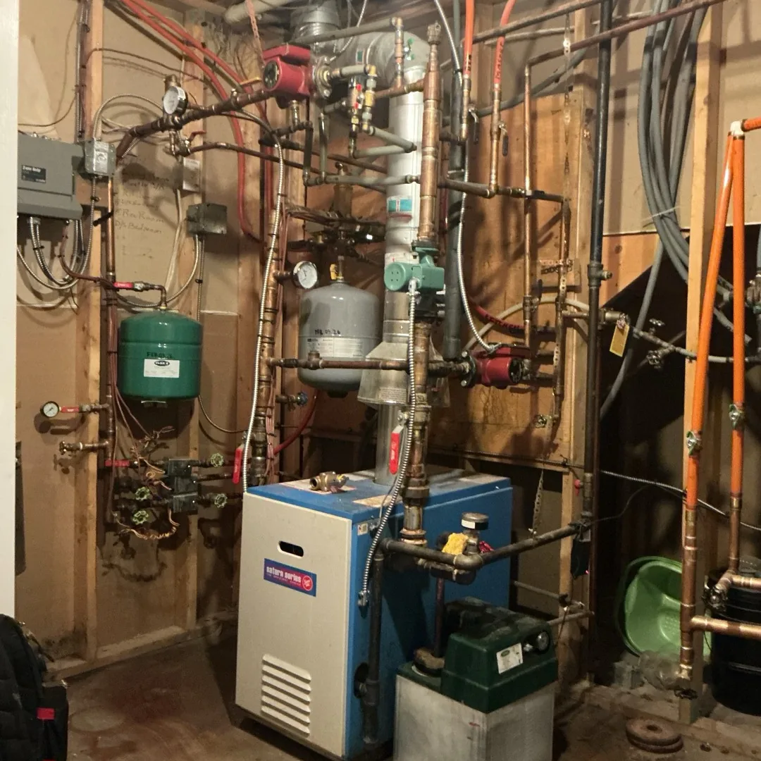 Aging residential boiler system in a Calgary basement before replacement by Arpi's, showing the original unit and years of added piping
