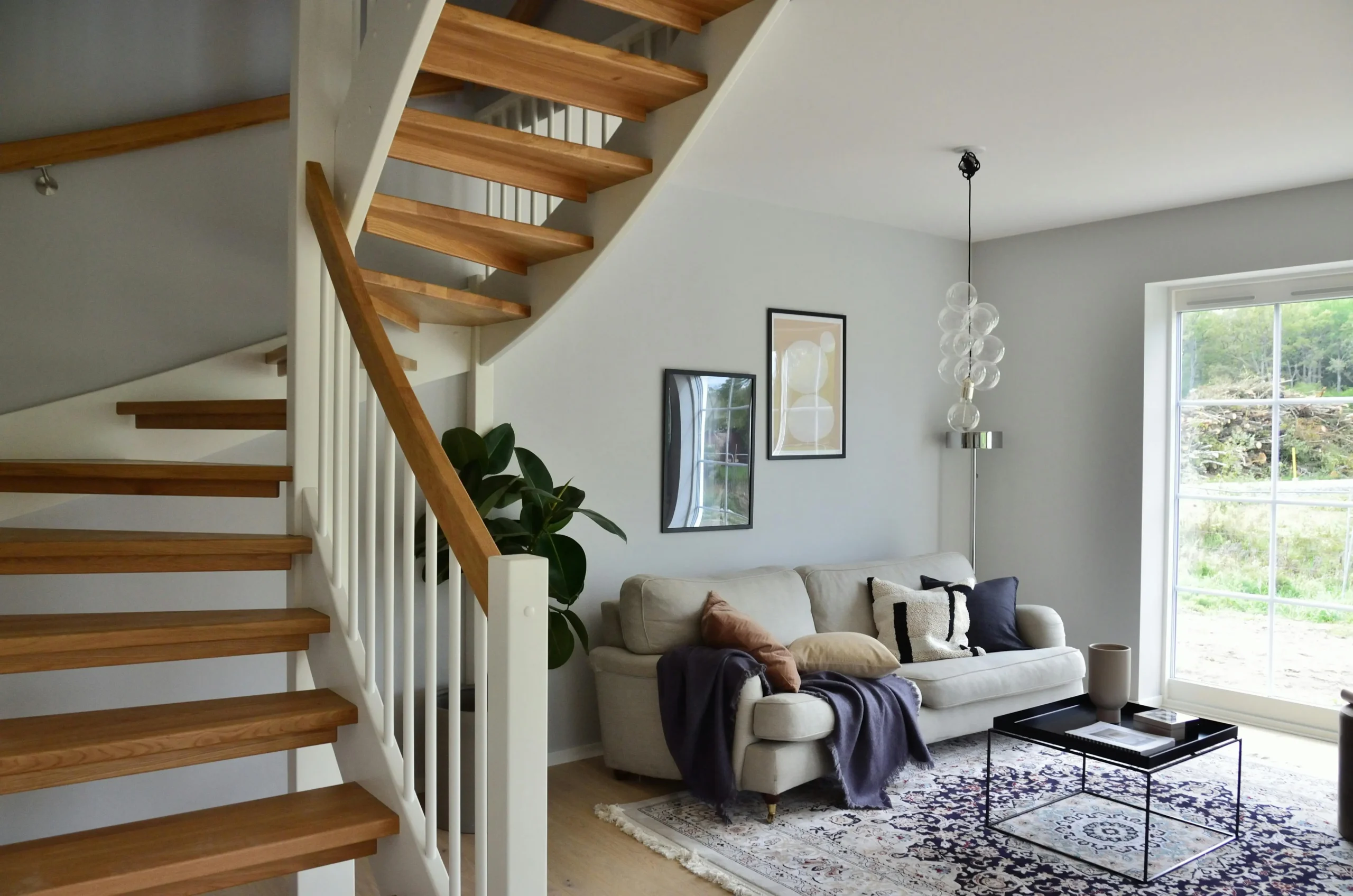 A cozy living room with sofa, staircase, cushions and a rug.