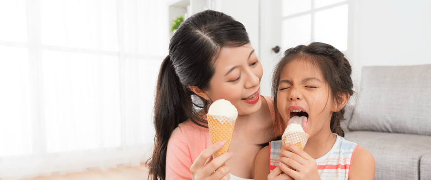 A mother and daughter enjoy ice cream in their air conditioned home.