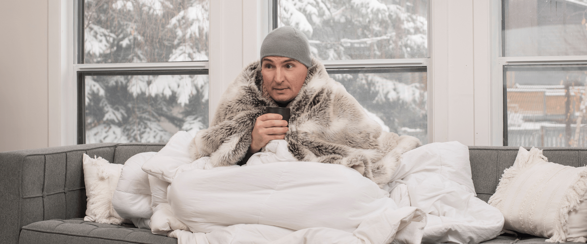 Calgary furnace quit so man sitting on couch in blankets and toque drinking coffee to stay warm
