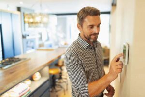 man turning on his furnace fan at home on the thermostat