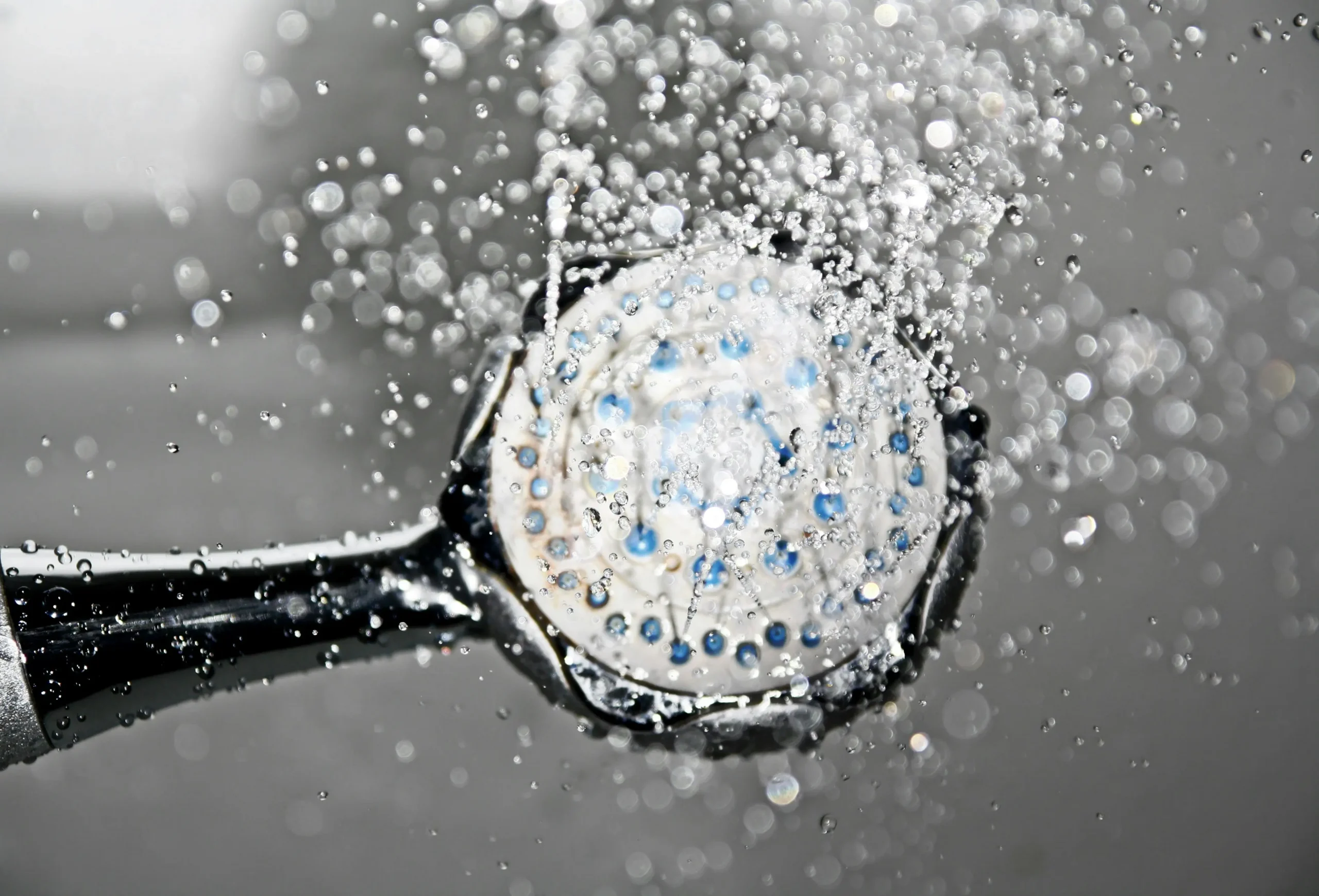 Close-up of a shower head spraying hot water, illustrating the steady, on-demand performance of Navien tankless water heaters installed by Arpis.