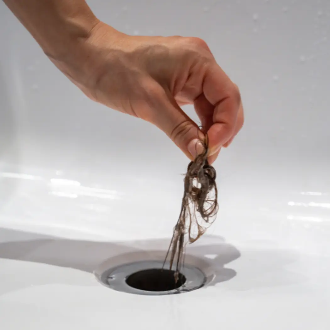 Hair clog being removed from a blocked shower drain — common cause of slow drains in Calgary homes