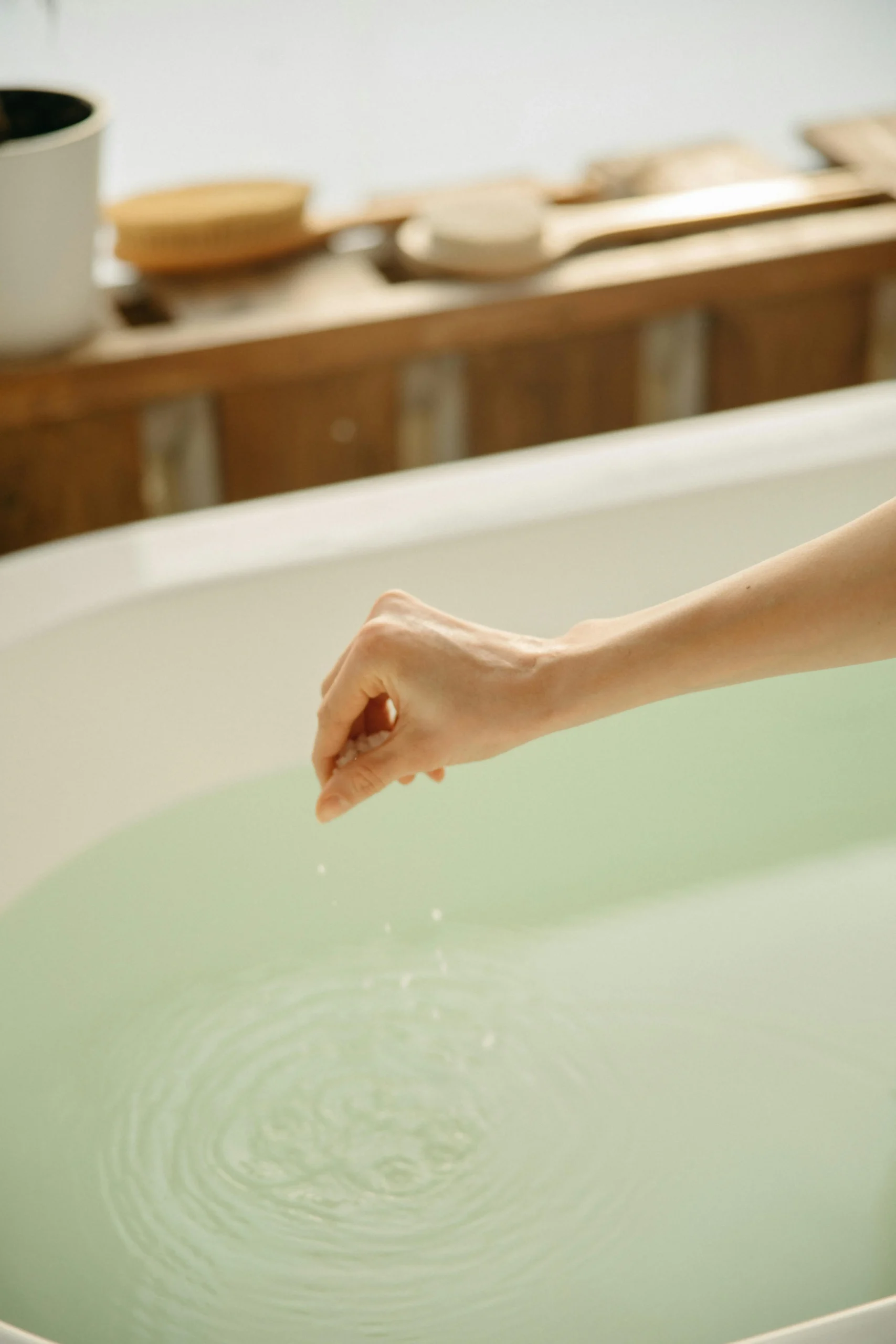 Hand sprinting bath salts into warm bath water, highlighting the consistent temperature and comfort provided by Arpis tankless water heaters.