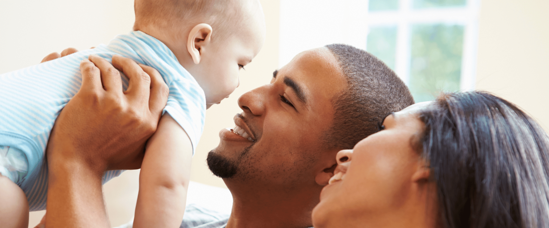 Father lifts baby in the air smiling while mom looks at baby with awe.