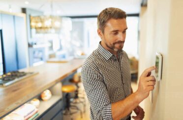 man turning on his furnace fan at home on the thermostat